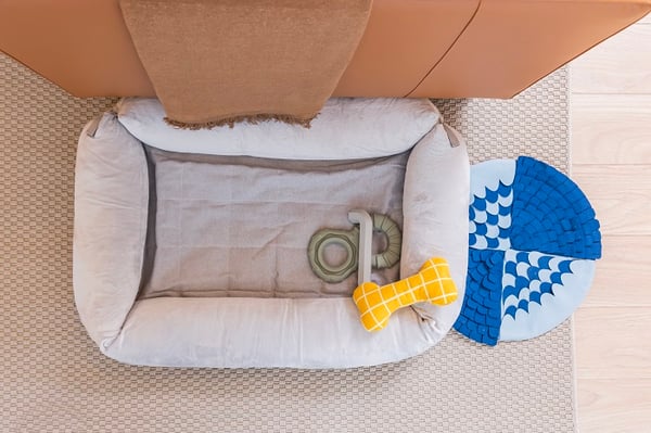 Cozy dog bed with plush toys placed on a beige carpet near a sofa.