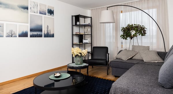 Cozy living room with gray sectional sofa, black armchair, and wall art of nature landscapes.