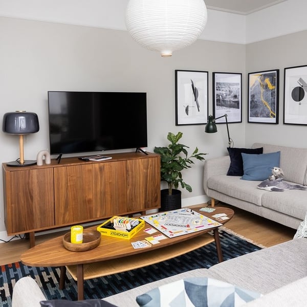 Cozy living room with grey sofas, wooden TV stand, framed wall art, and Monopoly board game on coffee table.