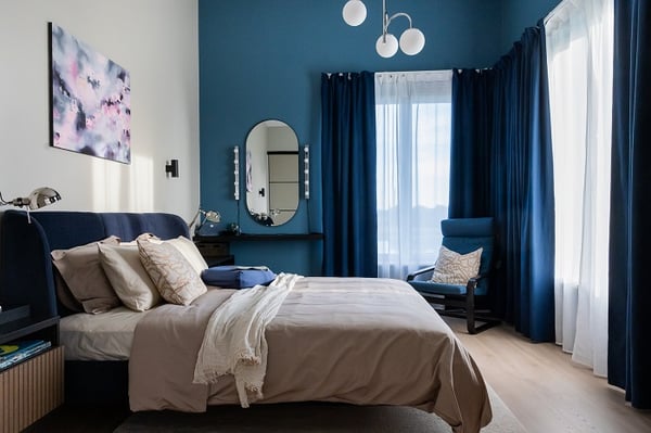 Cozy modern bedroom with blue accent wall, upholstered bed, and reading chair