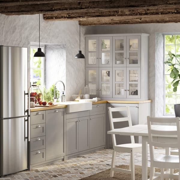 Cozy rustic kitchen with gray cabinets, farmhouse sink, stainless fridge, wood beams, and bright windows bringing in natural light.