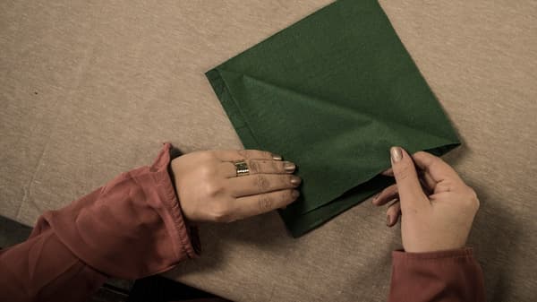 Crafting instructions, step 1: Turn a square napkin so that the flaps are facing upwards away from you. Fold each flap over with a margin of about 1 cm towards the edges.