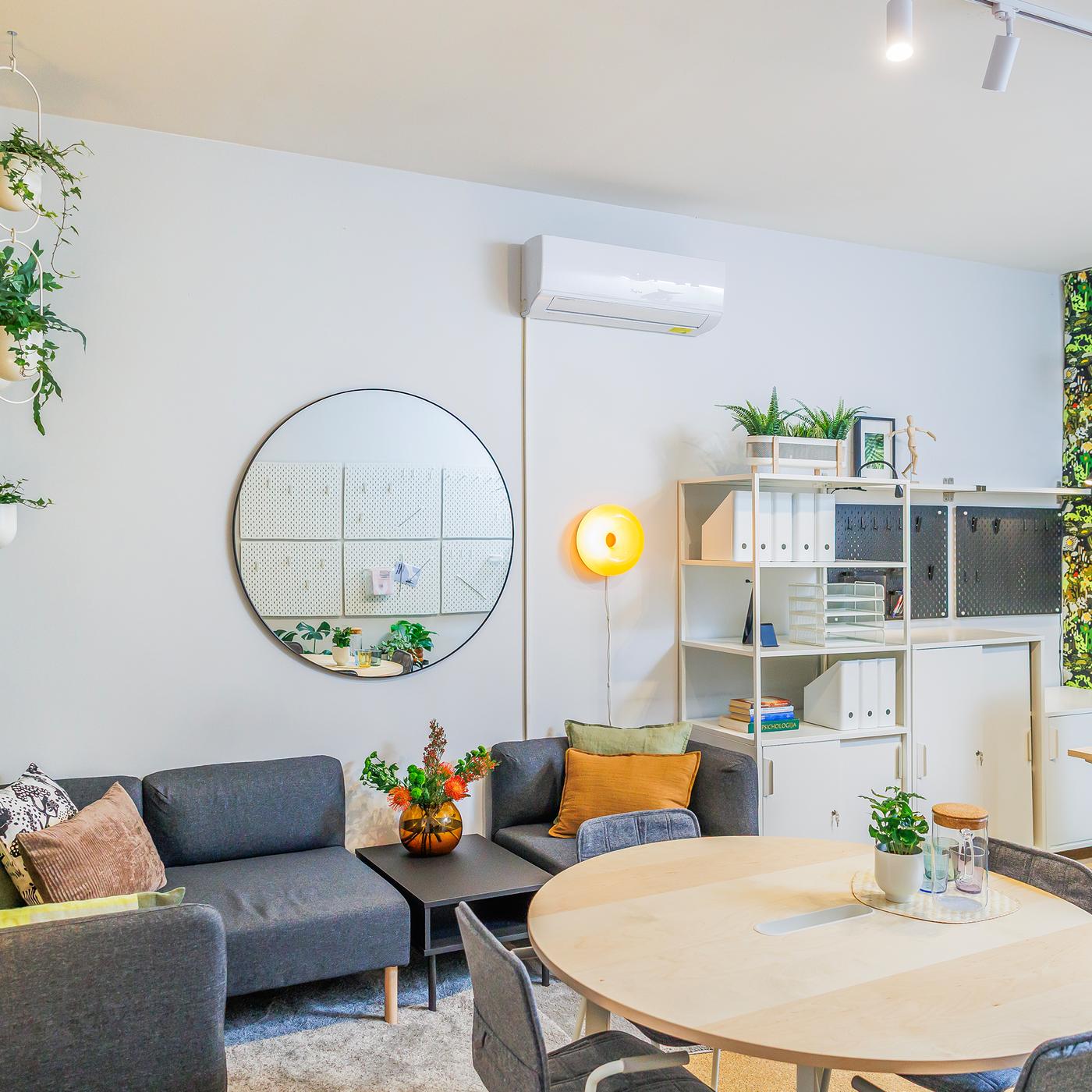 Crisis centre reception after the renovation: a warmly lit space featuring a sofa, light wood and white furniture, a mirror and indoor plants.