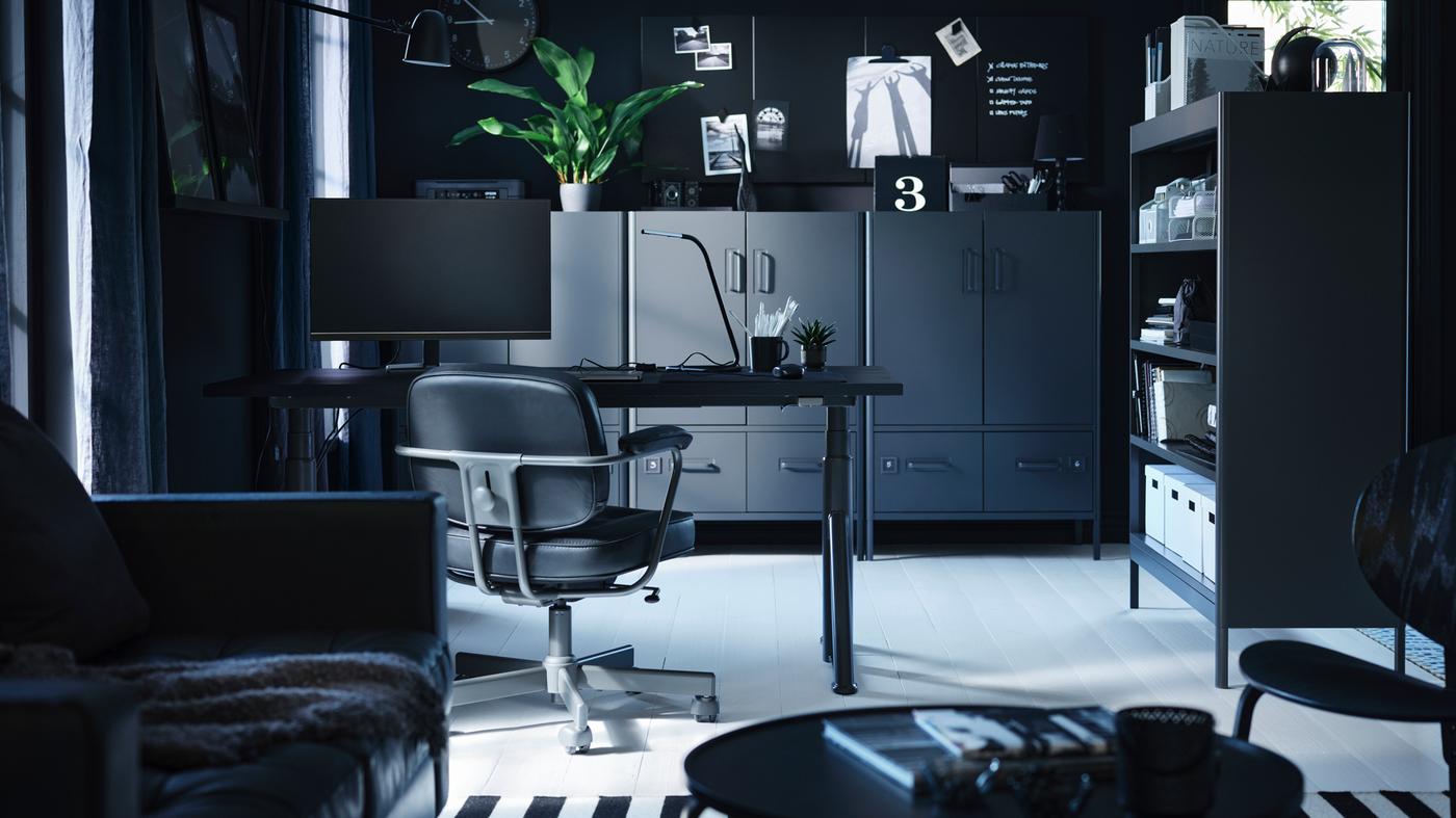 Crni/tamnosivi IDÅSEN stol za sjedenje/stajanje pored regala u tamnosivom kućnom radnom prostoru s elementima koji su postavljeni uz zidove.