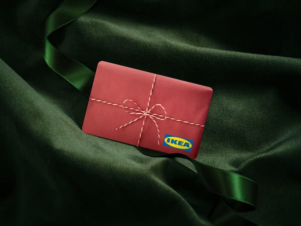Crvena poklon kartica IKEA na zelenoj svilenoj tkanini, omotana bijelim koncem.