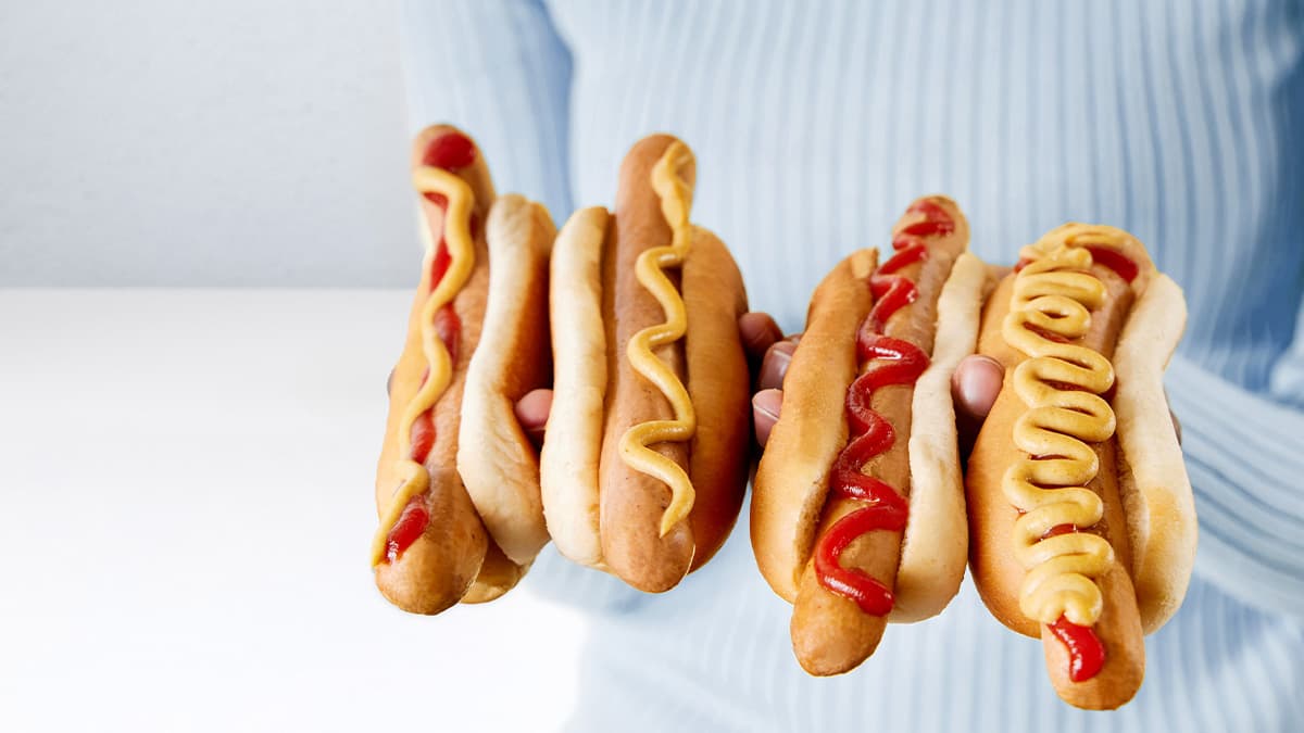 čtyři hot dogy s kečupem a hořčicí v rukách ženy v modrém