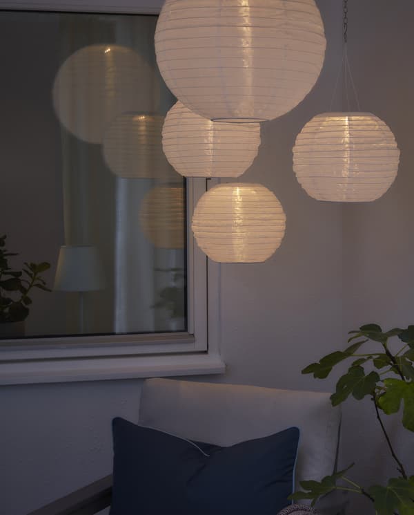 Čtyři kulaté, bílé, solární, závěsné lampy, které vytvaří útulné osvětlení v tmavém venkovním prostoru.