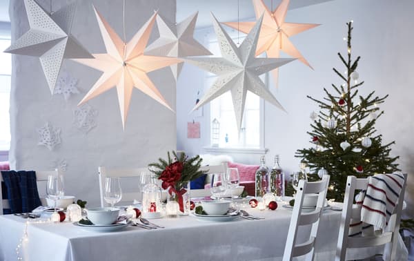Cuarto grande e luminoso con poucos mobles, agás unha longa mesa posta para unha celebración. Unha árbore de Nadal nun extremo e estrelas de papel no teito.