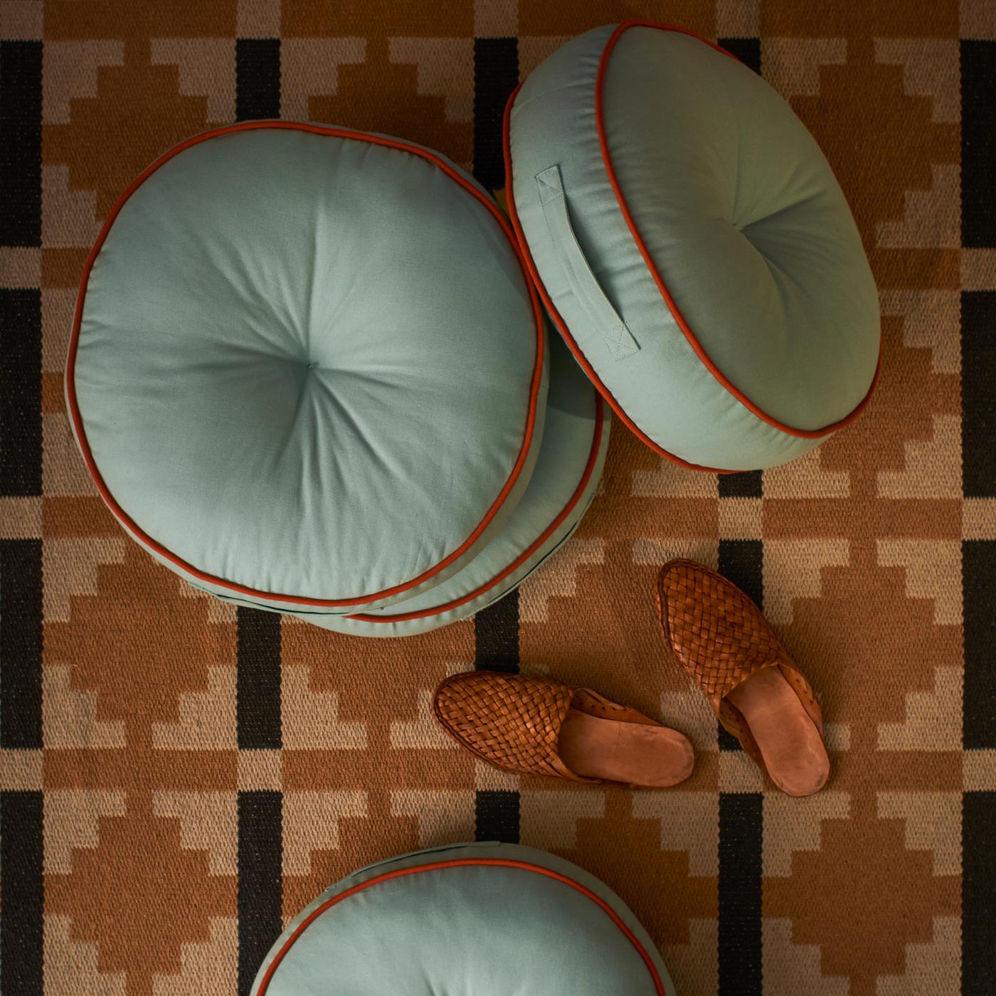 Cuatro cojines para suelo GOKVÄLLÅ y unas zapatillas de estar por casa sobre una alfombra.