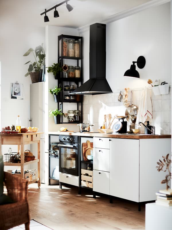 Cucina bianca e nera con dettagli in legno che scaldano l’ambiente: il piano di lavoro, il pavimento e il carrello FÖRHÖJA.
