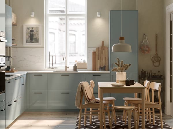 Cucina con frontali KALLARP, un tavolo RÖNNINGE con quattro sedie e una lampada a sospensione BUNKEFLO bianca con dettaglio in betulla.
