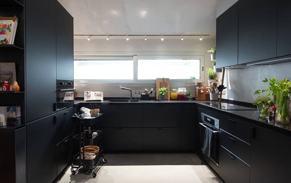 Cucina di colore nero con un carrello RÅSKOG, illuminata da luce su binari. Sul bancone ci sono diverse brocche con verdure fresche.