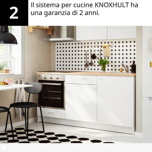 Cucina moderna con mobili bianchi, piano in legno, forno, motivo a pois, pianta e tappeto bianco e nero.
