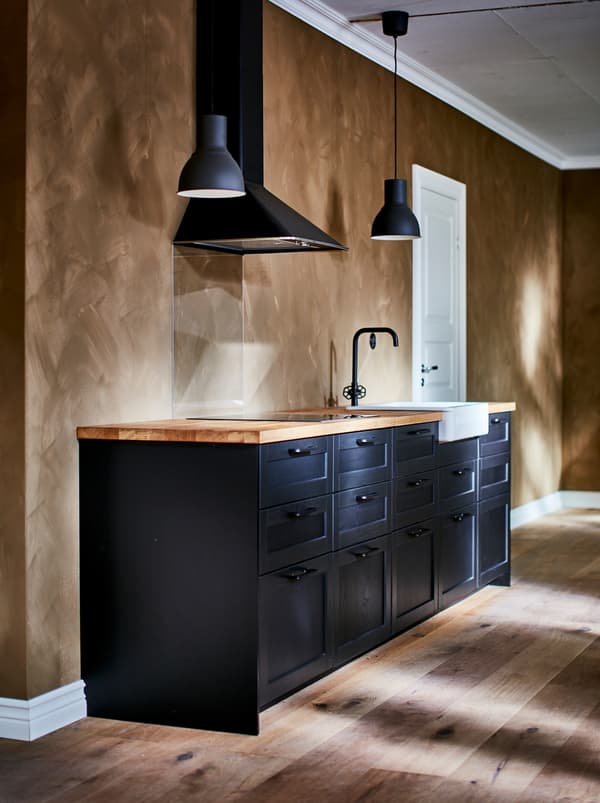 Cucina nera con lampade a sospensione HEKTAR grigio scuro, miscelatore nero e lavello HAVSEN bianco con frontale visibile.