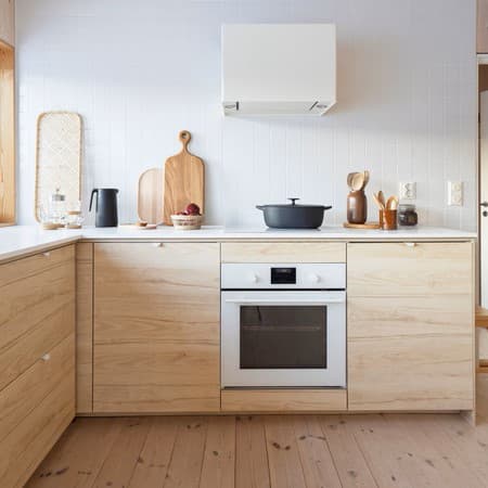 Cuina senzilla amb mobles de color fusta clara, un forn blanc, extracte i altres paraments de cuina.