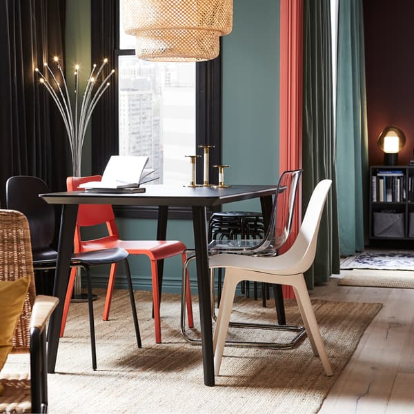 Cuisine avec coin repas comprenant une table noire, des chaises rouge, noire et blanche, une suspension en bambou ainsi qu’un tapis en jute.
