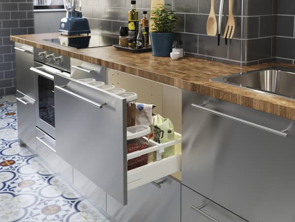 Cuisine en acier inoxydable avec plan de travail en chêne/plaqué. Un tiroir ouvert avec divers produits secs à l’intérieur.