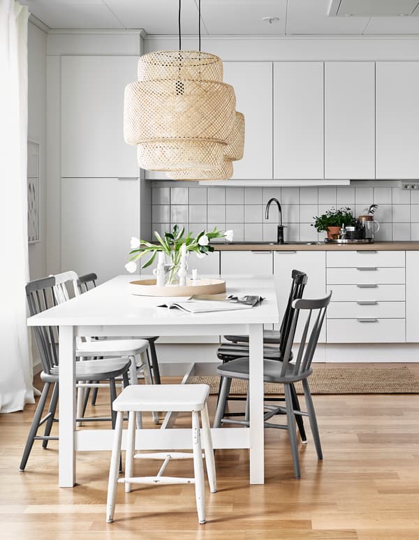 Cuisine en blanc et dans des couleurs neutres, avec grande table et chaises, décorée d'un simple bouquet de fleurs.