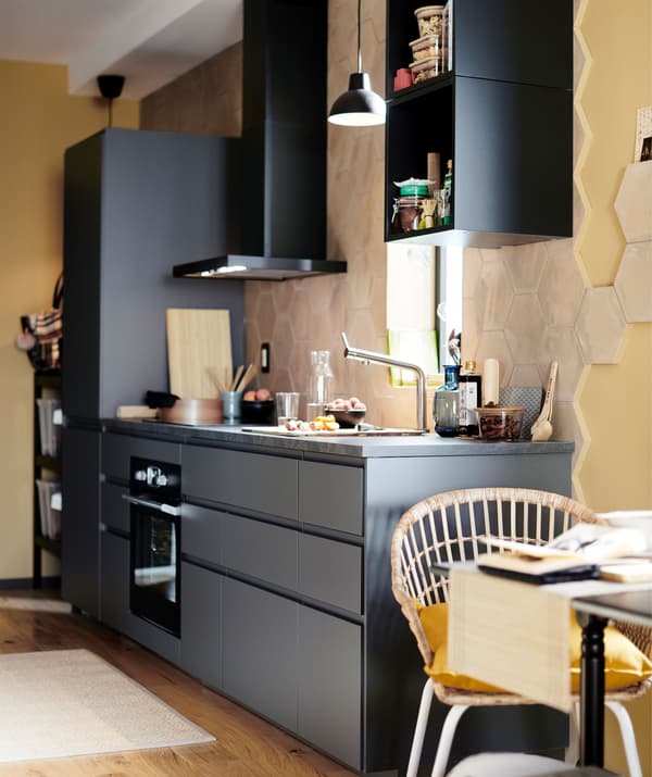Cuisine en finition noire avec hotte murale dans une zone peinte en jaune tendre.
