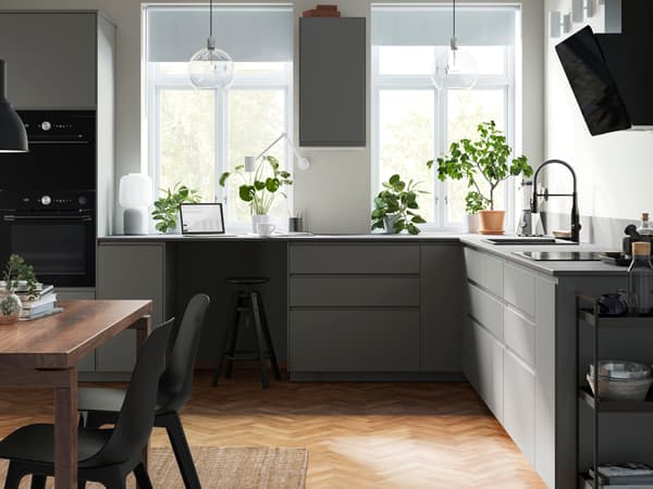 Cuisine gris foncé mat moderne avec un comptoir en pierre et des poignées intégrées. Cuisine en L, avec des électroménagers noirs et un modèle épuré à 2 tiroirs.