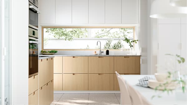 Cuisine très ensoleillée avec des fenêtres donnant sur un jardin. Les façades de cuisine FRÖJERED en bambou sont associées à des façades blanches.