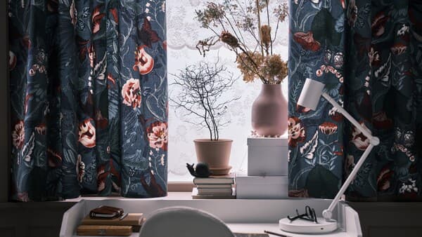 Curtains made with dark blue/floral FILODENDRON fabric in a window above a white HAUGA desk with a white NYMÅNE work lamp.