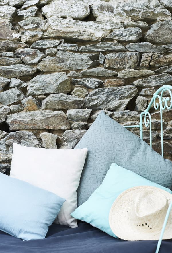 Cushions in different shades of blue against an old brick wall.