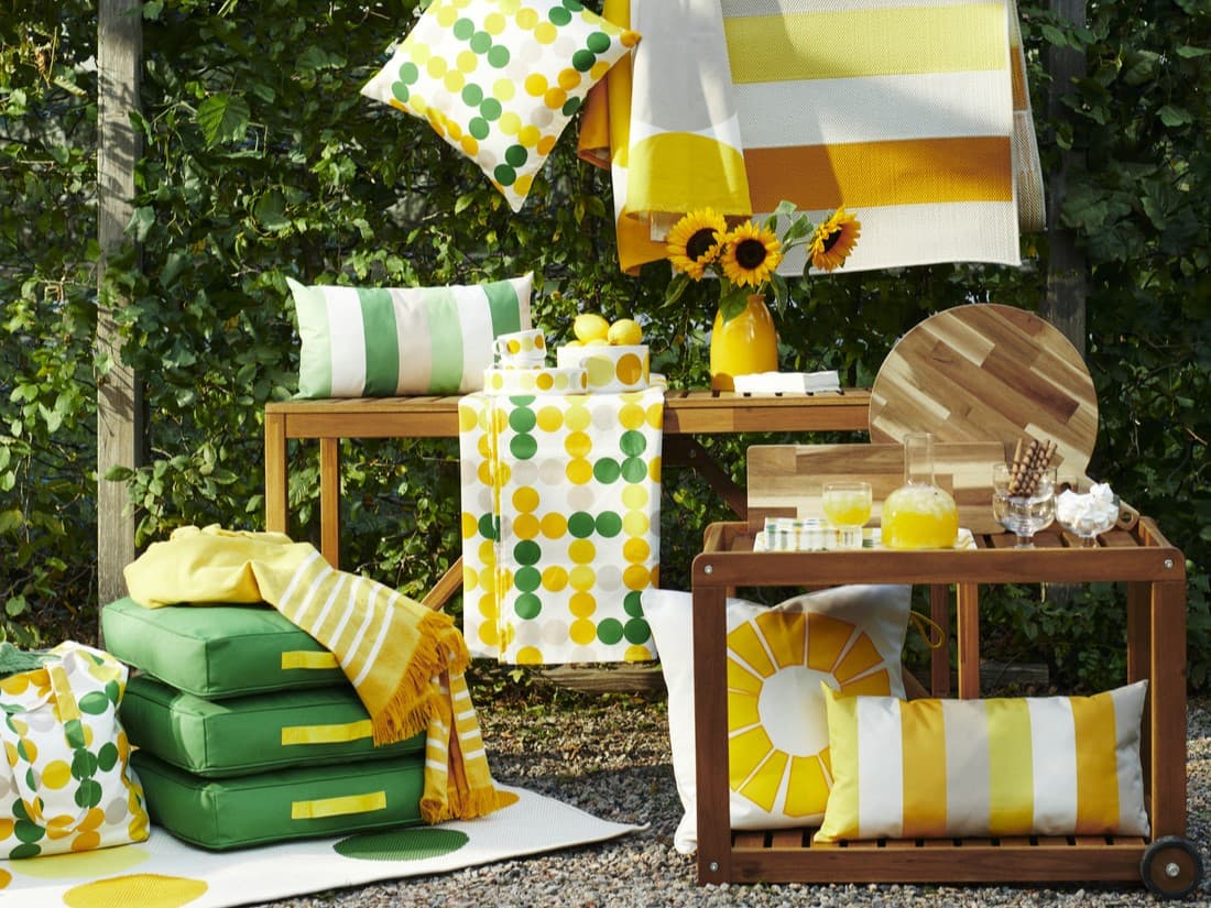 cushions, linen in yellow and green patterns of BRÖGGAN collection displayed on tables backed by greenery
