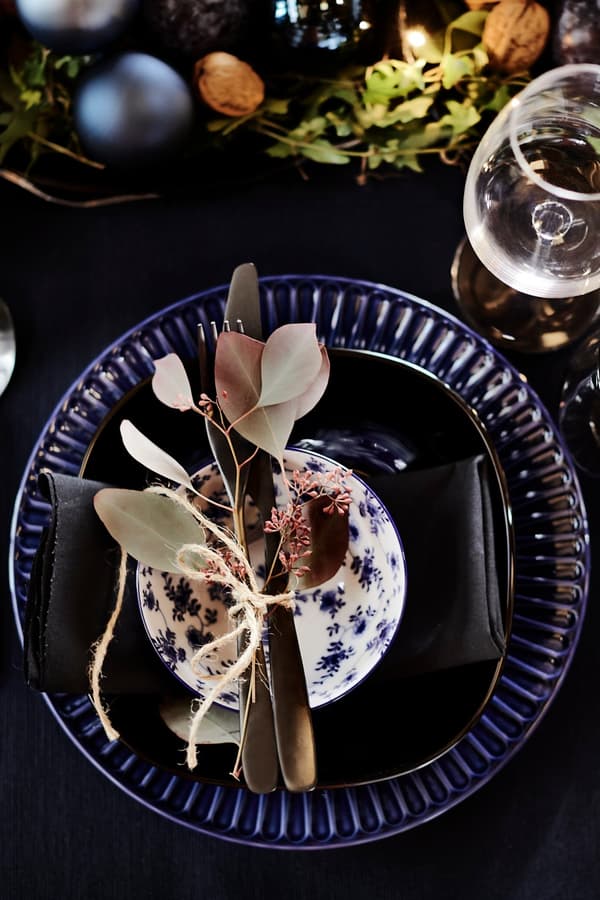 Cutlery decorated with eucalyptus branches placed on a dark blue plate.