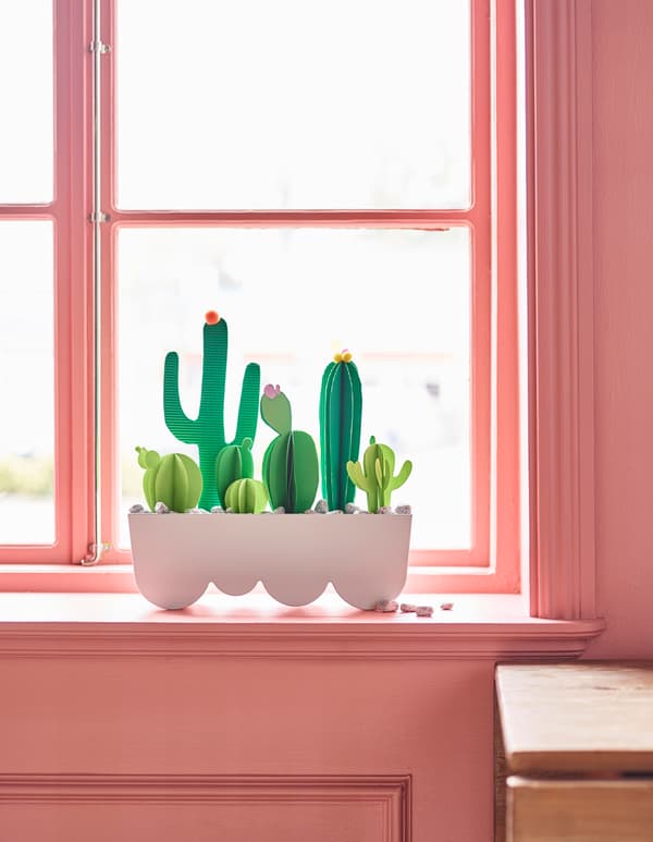 Cutouts of cacti in a plant pot sit in a window.