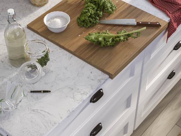 Cutting board with chopped kale, a knife, and jars on a kitchen countertop.