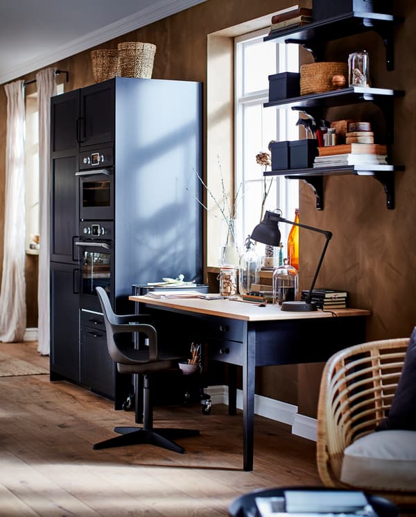 Czarne biurko z sosnowym blatem, krzesło obrotowe, czarnobrązowe półki ścienne i fragment czarnej kuchni z szufladami i drzwiami.