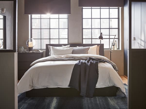 Czarnobrązowa, wysoka rama łóżka IKEA MALM ma elegancką okleinę i nowoczesny design oraz proste linie i krawędzie. Komplety pościeli BLÅVINDA i KUNGSBLOMMA dodatkowo złagodzą jej wygląd.