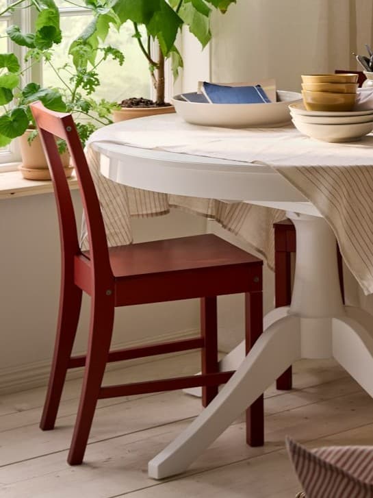 Czerwone krzesło stojący przy białym, okrągłym stole w jasnej jadalni.