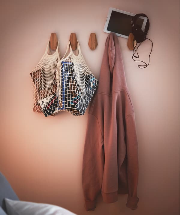 Część ściany w sypialni z rzędem bambusowych haczyków SKUGGIS z pełnymi siatkami, bluzą z kapturem i tabletem ze słuchawkami.