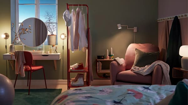 Dæmpet stemningsbelysning i et soveværelse med en makeupstation, et garderobestativ, brugt som rumdeler, og en læsekrog med hvilestol.
