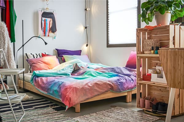 Dans un coin de l’appartement, lit deux places, portant et étagère composée de caisses en bois