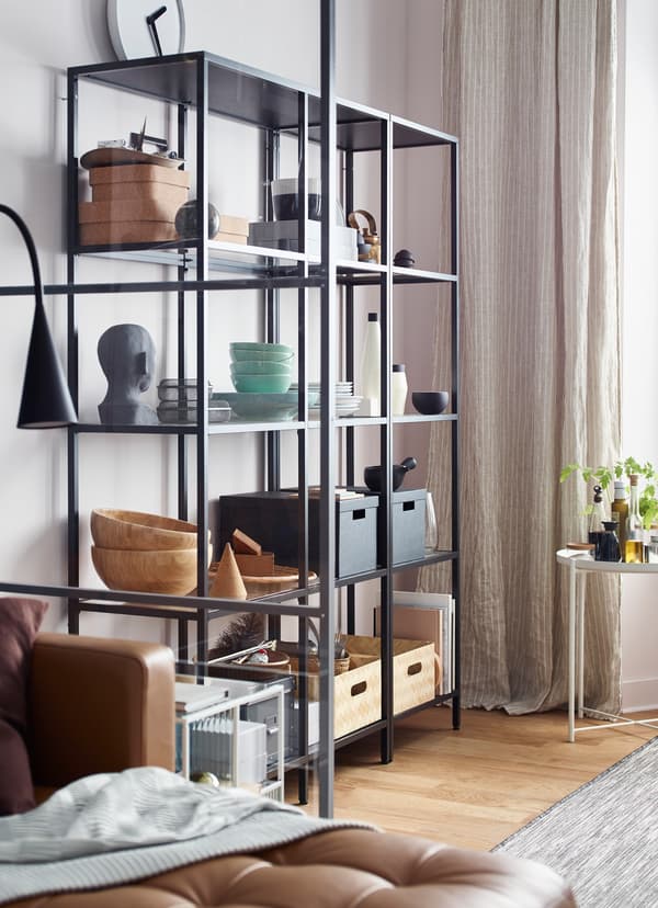 Dans un coin repas, des boîtes, coupes et statues sont disposées sur une étagère fil noire.