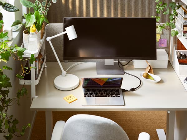 Dans un espace de travail moderne et lumineux, bureau TROTTEN en beige/blanc entouré de plantes vertes en pot.
