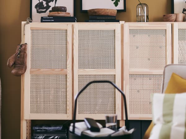 Dans un salon, deux armoires IVAR en pin naturel avec portes en cannage de bambou. Livres et objets déco sur l’une d’elles.