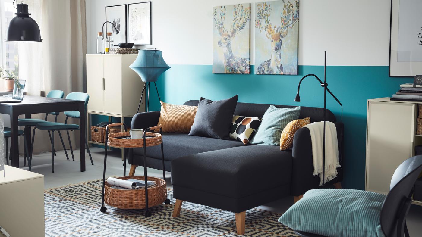 Dans un salon ensoleillé aux tons bleus et gris, canapé LINANÄS avec méridienne gris foncé, devant une desserte en rotin.