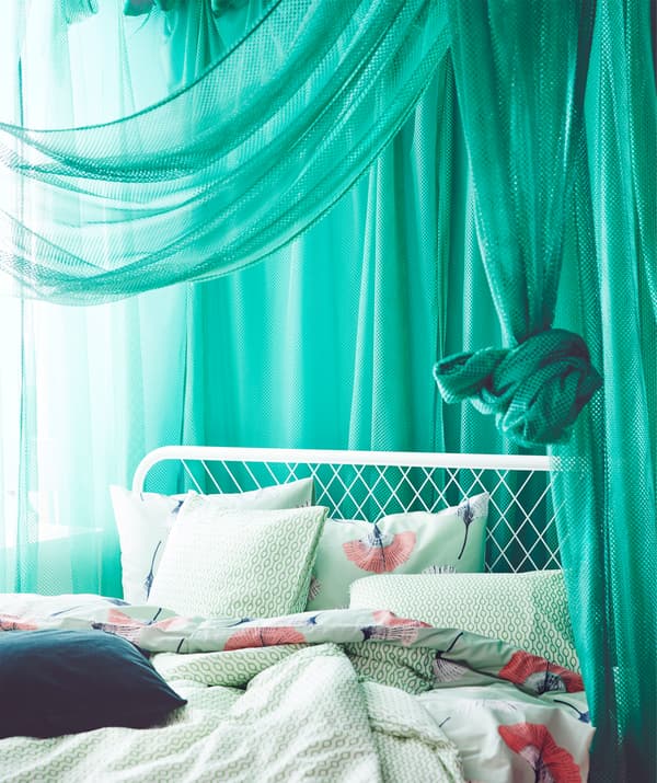Dans une chambre à coucher, de fins voilages verts IKEA GRÅTISTEL laissant passer un peu de lumière.