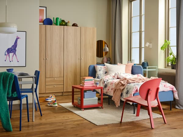 Dans une chambre à coucher lumineuse et colorée, lit avec tête de lit d’angle BLÅKULLEN bleu moyen revêtu de linge de lit LAPPNYCKLAR.