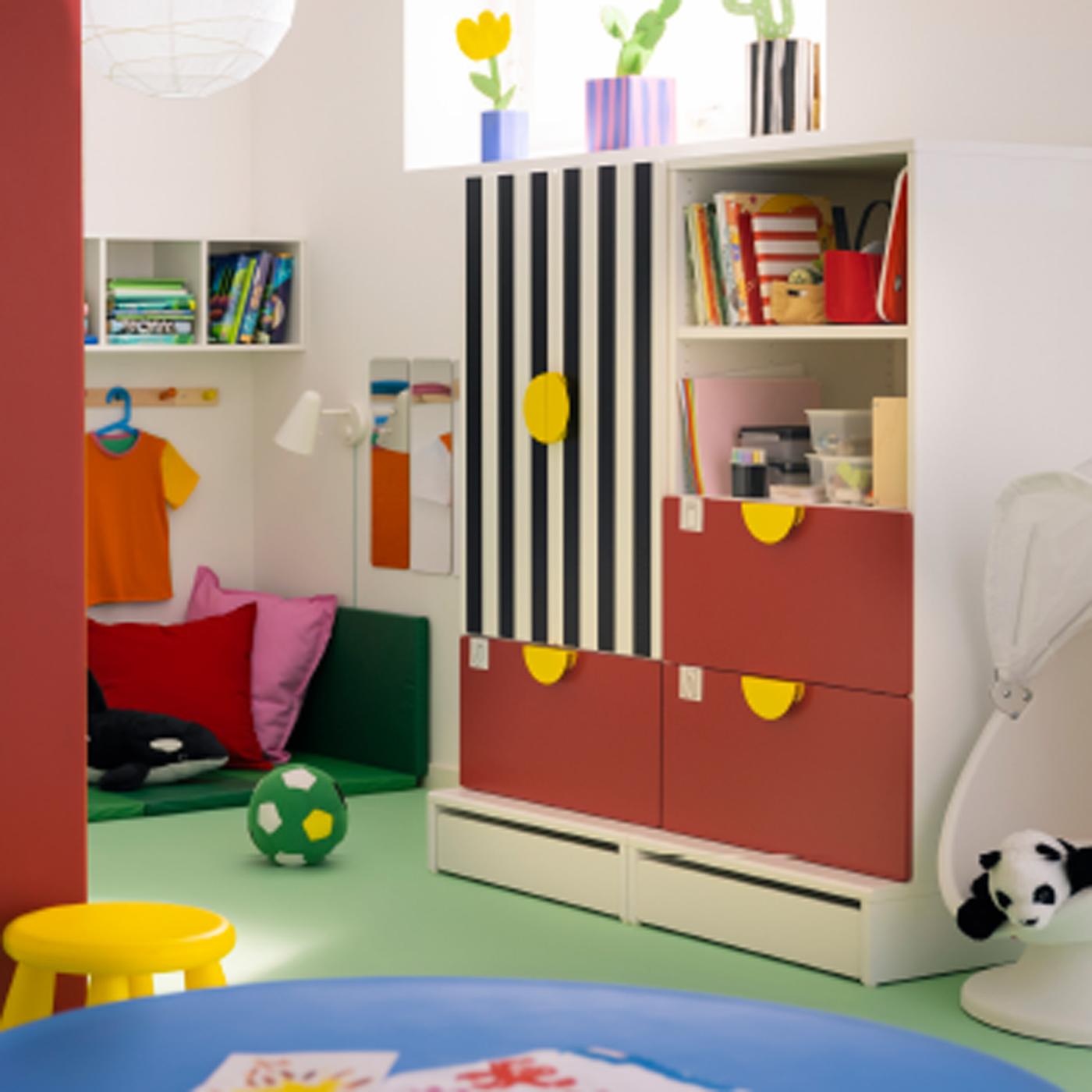 Dans une chambre d’enfant aux murs blancs, rangement SMÅSTAD/PLATSA rouge et à rayures avec trois tiroirs.