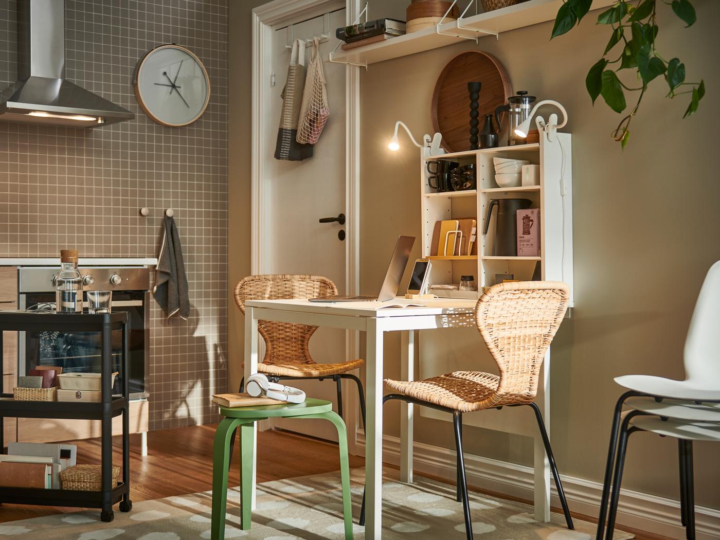 Dans une cuisine lumineuse, une table MELLTORP blanche est entourée de différents sièges, dont des chaises ÄLVSTA avec assise en rotin et structure noire.