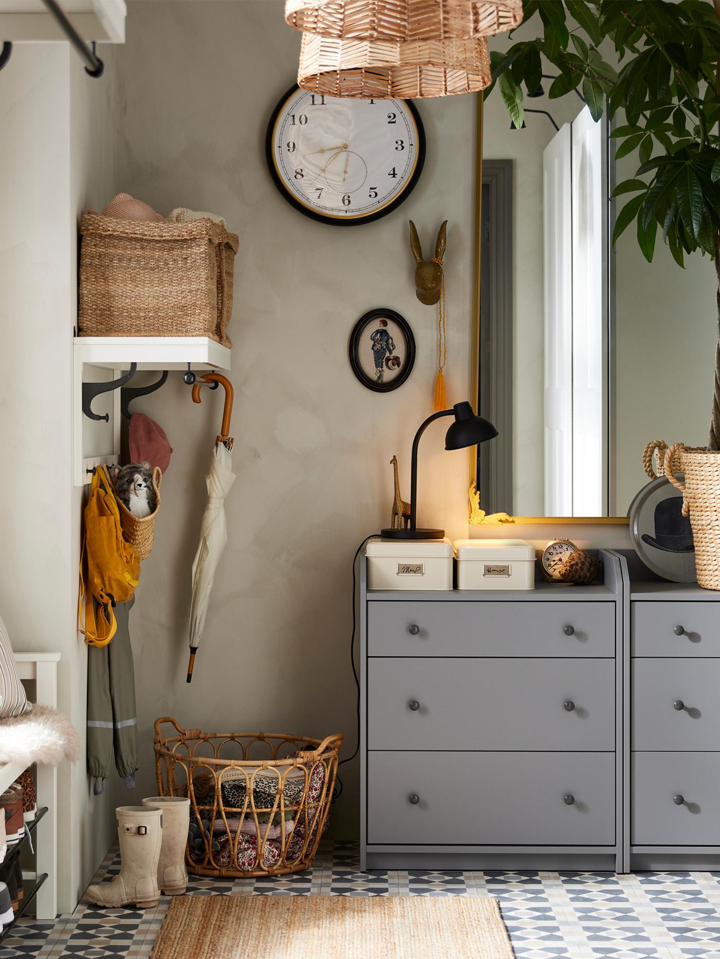 Dans une entrée, deux commodes 3 tiroirs HAUGA en gris, avec un tapis LOHALS devant, et un miroir et une horloge au-dessus.