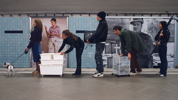 Dans une gare, une longue file de personnes où chacune porte des meubles à la main.