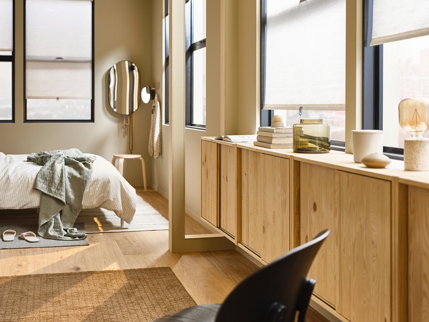 Dans une grande chambre à coucher, lit installé dans un coin, miroir LINDBYN fixé au mur et éléments IVAR en pin sous les fenêtres.