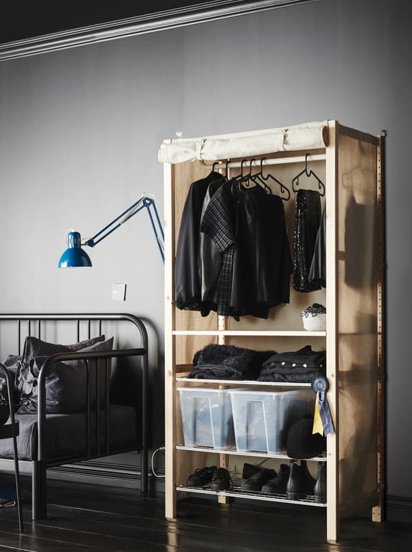 Dans une pièce minimaliste grise, un morceau de tissu transforme une étagère IVAR en une garde-robe remplie de vêtements.