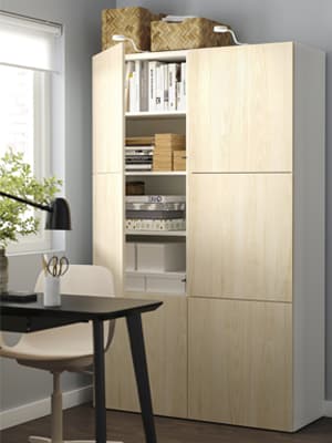 Dans une salle à manger, une table noire devant un meuble de rangement BESTA avec des portes FÄNRIK en bois entre ouvertes. 